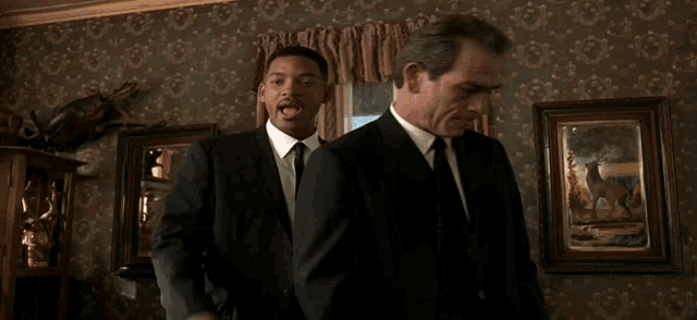 two men in suits are standing next to each other and talking