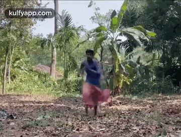 a man in a blue shirt and a red skirt is standing in a field .