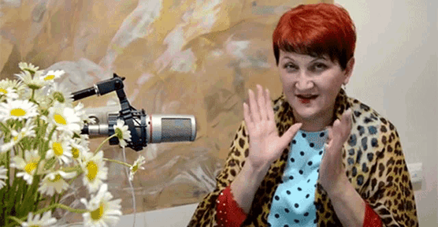 a woman with red hair is sitting in front of a microphone and flowers .