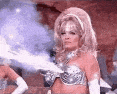 a woman in a silver bra and gloves is standing in front of a blue light .
