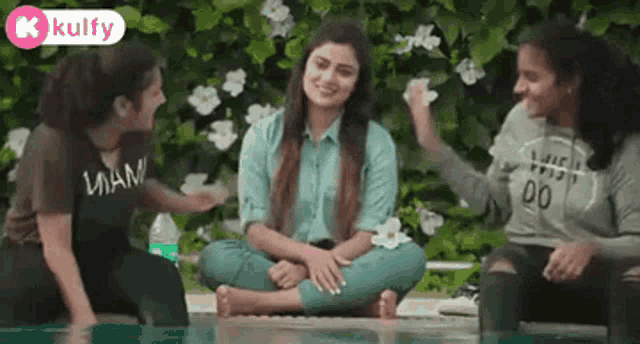 three girls are sitting on the ground next to a swimming pool .