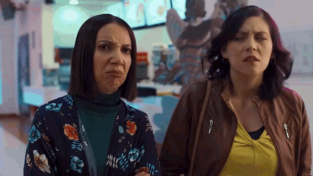 two women are standing next to each other in a hallway and one of them is making a face