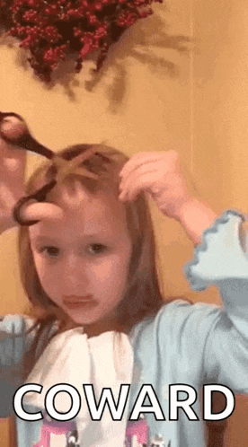 a little girl is cutting her hair with scissors and the word coward is on the bottom of the picture .