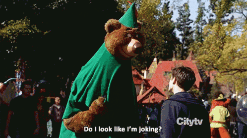 a man wearing a citytv sweatshirt stands next to a teddy bear