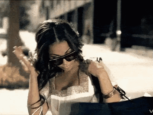 a woman wearing sunglasses is holding a bag and looking at something