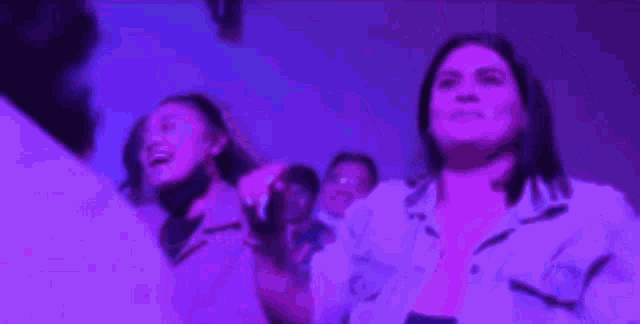 a woman is singing into a microphone in front of a crowd of people in a purple room .