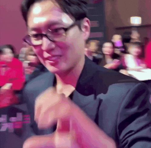 a man wearing glasses and a black suit is giving a thumbs up