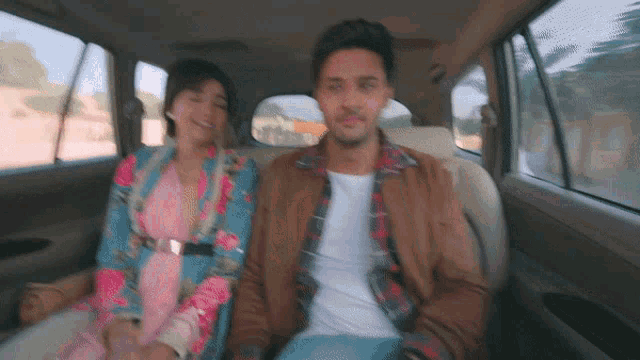 a man and woman sit in the back seat of a car