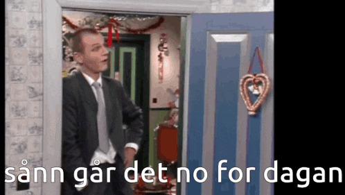a man in a suit and tie is standing in front of a blue door with a heart hanging from it ..