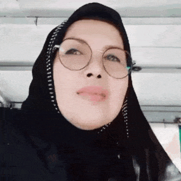 a woman wearing a hijab and glasses is smiling for the camera
