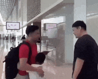 two men are standing next to each other in an airport talking to each other .