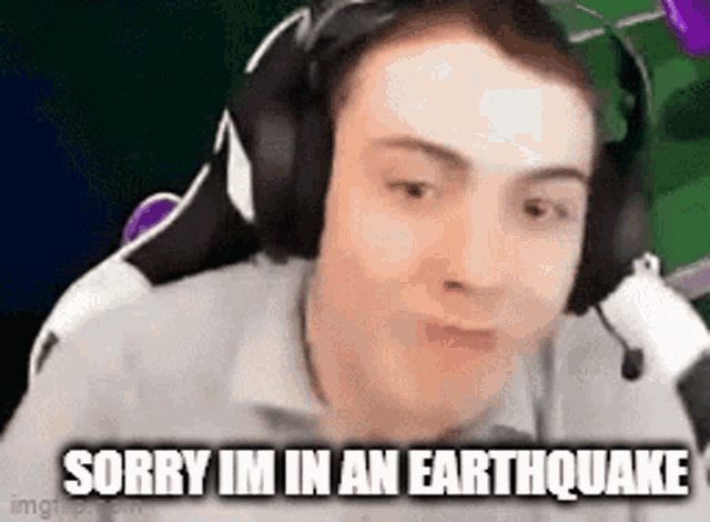 a man wearing headphones and a microphone is making a funny face and saying sorry im in an earthquake .