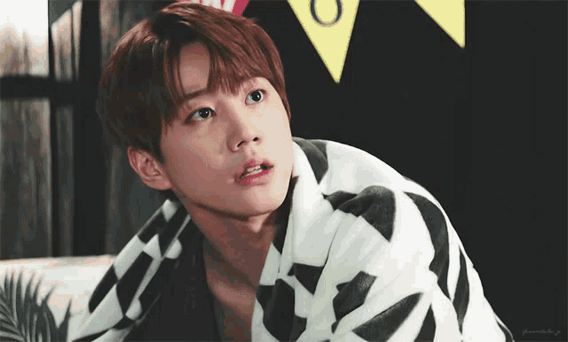 a young man wrapped in a blanket looks at the camera