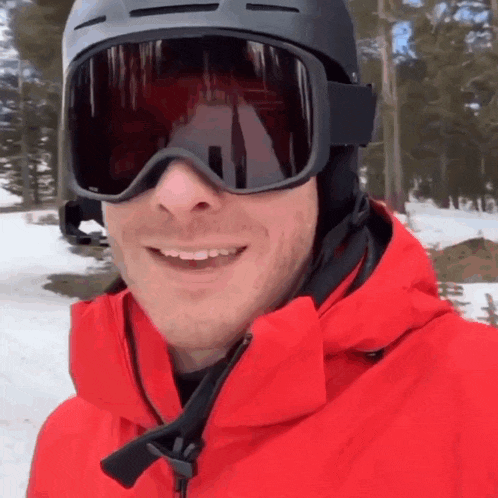 a man wearing ski goggles and a red jacket smiles for the camera
