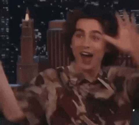 a young man in a camouflage shirt is making a funny face while holding his hands up in the air .