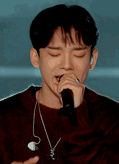 a young man is singing into a microphone with his eyes closed and a necklace around his neck