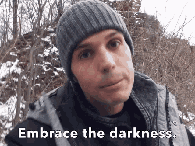 a man wearing a beanie and a jacket with the words embrace the darkness below him