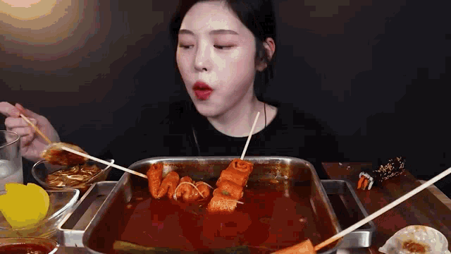 a woman is sitting at a table eating food with chopsticks from a pan .