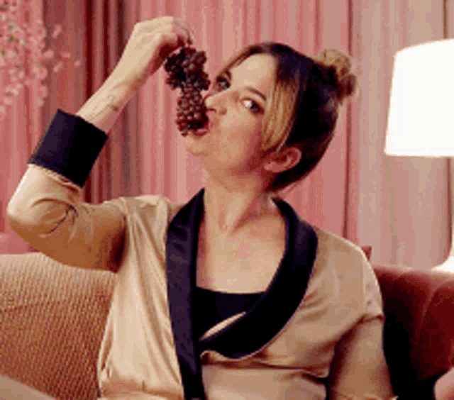 a woman is sitting on a couch and eating a bunch of grapes