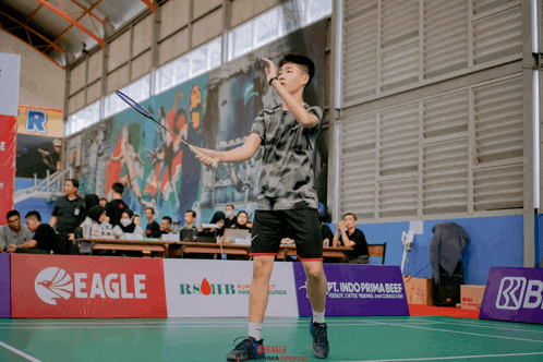 a boy is playing badminton on a court with a banner that says eagle on it