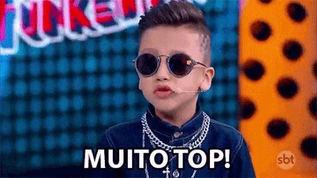 a young boy wearing sunglasses and a chain around his neck is talking into a microphone .