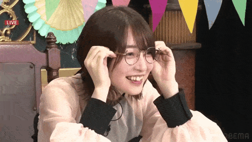a woman wearing glasses is smiling in front of a live screen that says abema