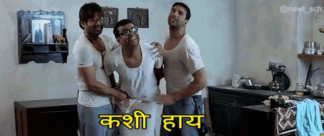 three men are hugging each other in a kitchen and one of them is wearing glasses