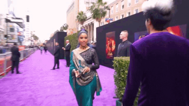 a woman in a blue and black dress walks down a purple carpet
