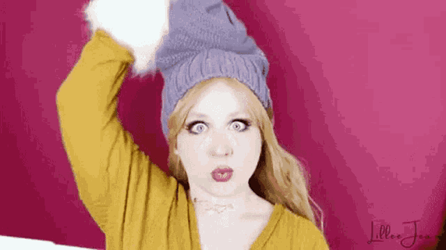 a woman wearing a yellow sweater and a purple hat is making a surprised face