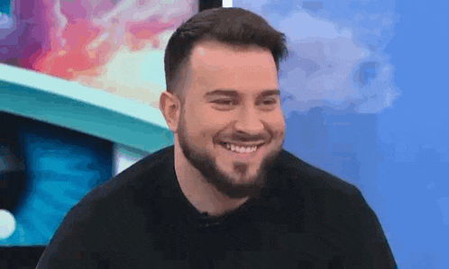 a man with a beard is smiling while sitting in front of a blue wall .