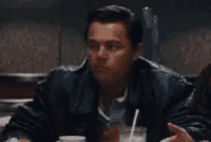 a man in a leather jacket is sitting at a table with a drink and a straw .