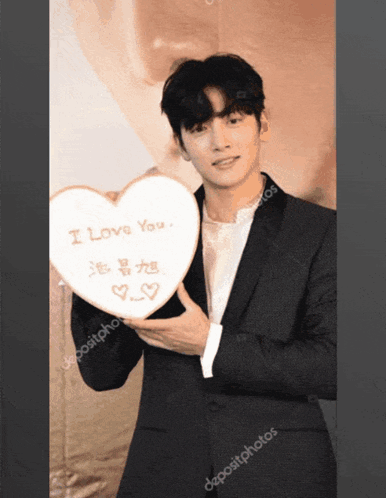 a man in a suit is holding a heart shaped sign that says " i love you "
