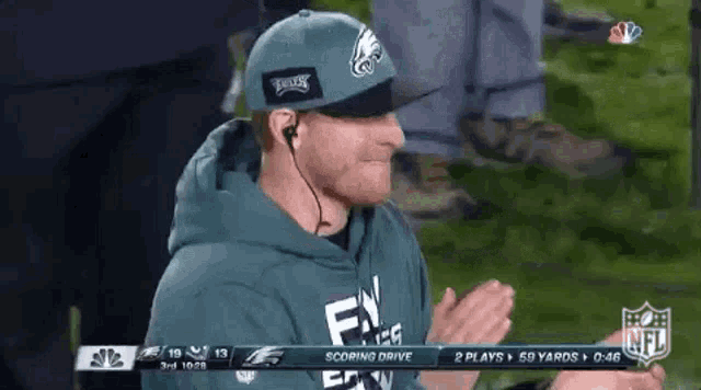 a man wearing a philadelphia eagles hat and a hoodie is clapping during a football game .