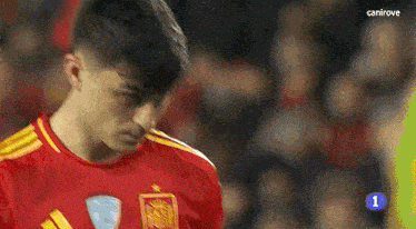 a soccer player wearing a red and yellow jersey with the number 1 on it is looking down .