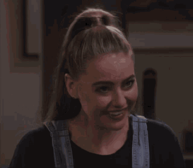 a woman wearing overalls and earrings is smiling