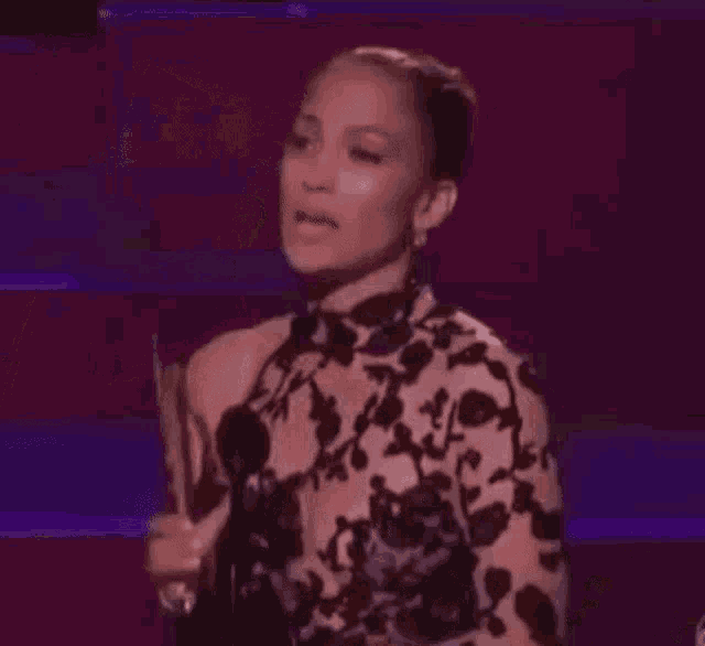 a woman in a floral dress is standing on a stage and holding a microphone .