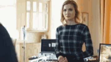 a woman in a plaid shirt is standing in front of a computer screen .