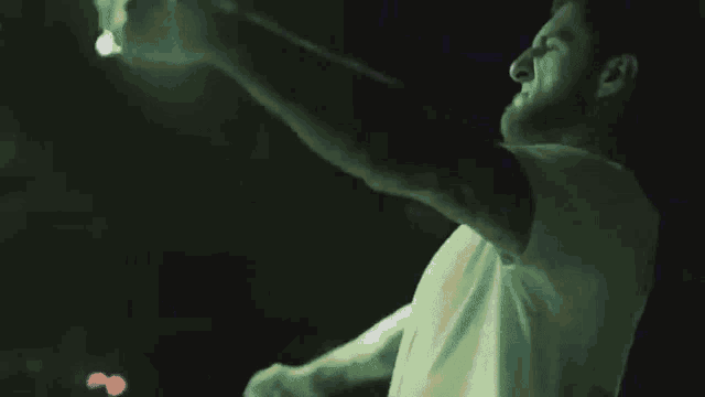 a man in a white shirt is singing into a microphone in a dark room .