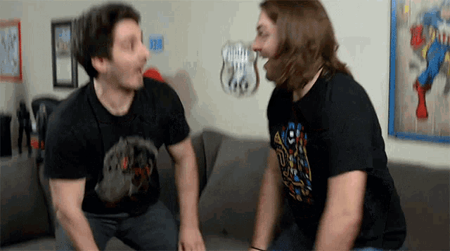 two men sitting on a couch with one wearing a shirt that says ' avengers '