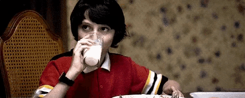 a young boy is sitting at a table drinking milk from a glass .