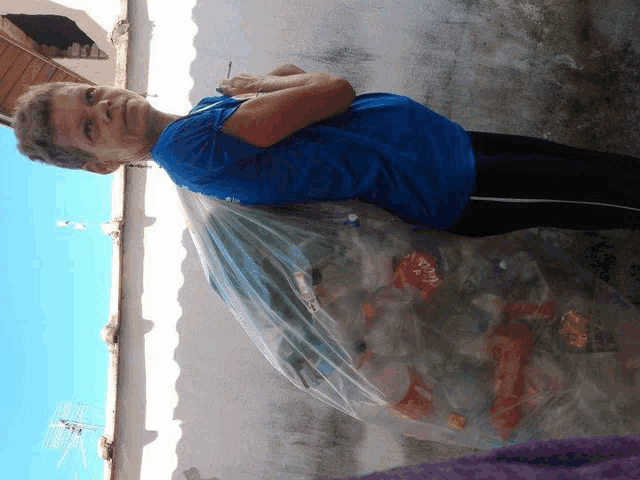 a woman in a blue shirt is carrying a plastic bag filled with coca cola bottles