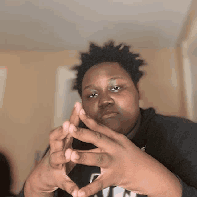 a man wearing a black shirt with the letter n on it holds his hands together