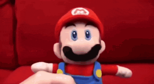 a mario doll is sitting on a red couch and giving the middle finger