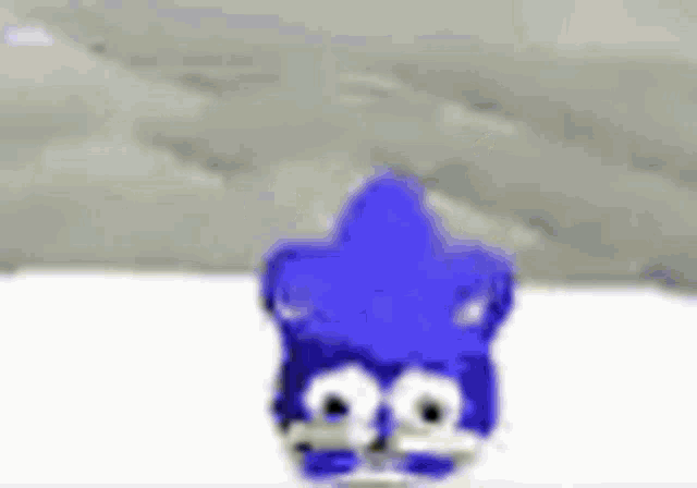 a blue cartoon character is standing in the snow with a mountain in the background .
