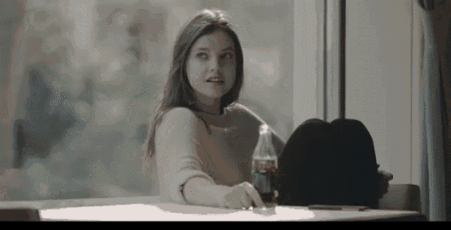 a woman is sitting at a table with a bottle of coca cola .
