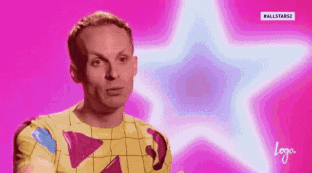 a man in a yellow shirt is standing in front of a pink background with a star in the background .
