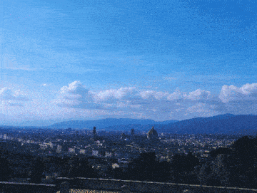 a cityscape with mountains in the background and a blue sky with clouds