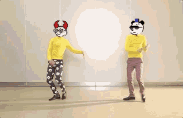 two men are dancing in front of a wall and one has a devil mask on his head