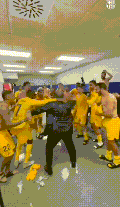 a group of soccer players in yellow uniforms are dancing in a locker room
