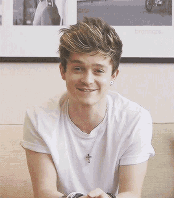 a young man wearing a white shirt and a cross necklace smiles for the camera